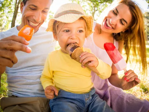 Family of three, sitting on the ground eating popsicles