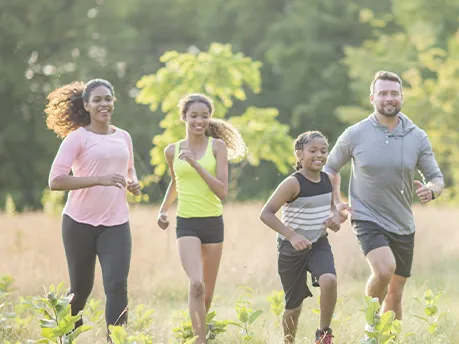 A family of four, running together outside in a field.