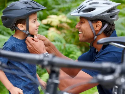 A dad adjusts his son's helmet before a bike ride