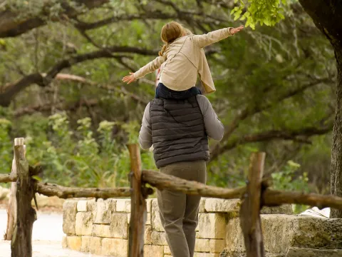 Father and daughter walking in the woods next to a fence.