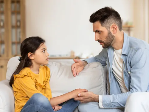 A father talks with his daughter while both are sitting on a couch.