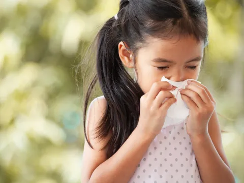 A little girl blows her nose into a tissue.