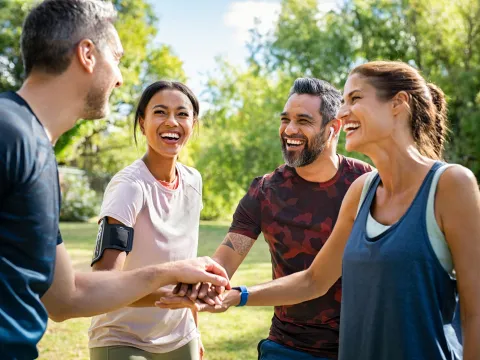 Group of active mature friends in park stacking hands after workout - stock photo