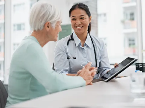 A Physician Smiles While She Goes Over a Patient's Chart With Her on a Tablet