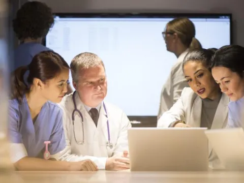 Doctors Huddle Around a Laptop Going Over Research