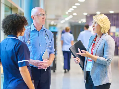 A CPE Pastor Speaks with a Doctor and Nurse in the Hallway of a Hospital.