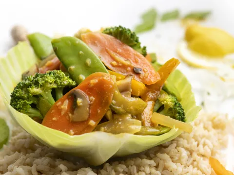 Lettuce bowl filled with veggie stir-fry sitting on brown rice