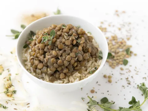 Bowl of lentils and rice on white surface with green garnish