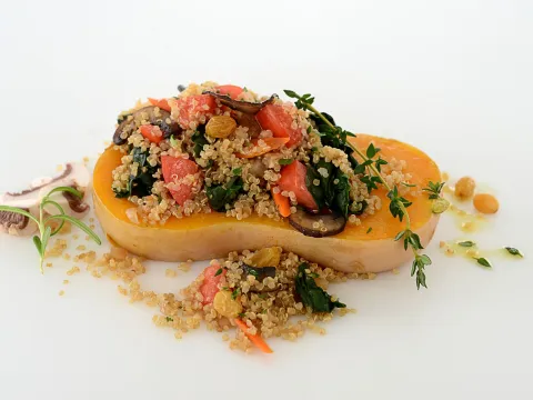 Quinoa, mixed with plum tomatoes, Swiss chard and mushrooms, placed in the center of a butternut squash half