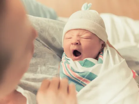 A mom carrying her new born baby. The new new born baby is yawning