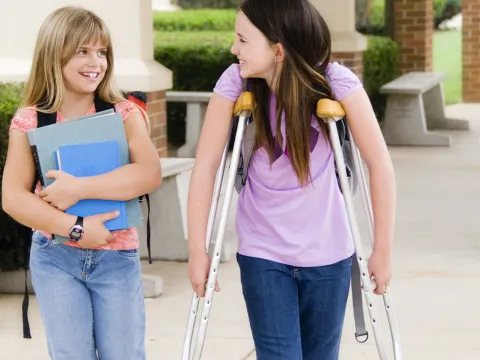 A girl on crutches walks with her friend at school