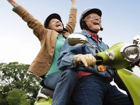 A joyful couple takes a ride on a scooter.