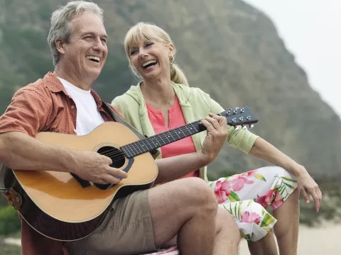 A couple playing guitar on the beach.