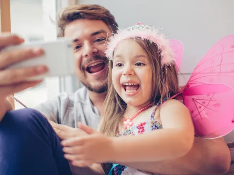 A dad and daughter take a selfie while playing dress up.