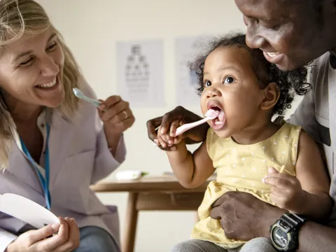 A dentist helps a father teach his daughter to brush her teeth