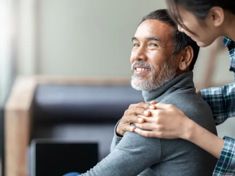 A daughter hugs her father from behind.