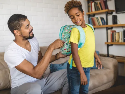 A father adjusts his child's backpack.