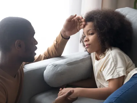 A black man checks his daughter for a fever