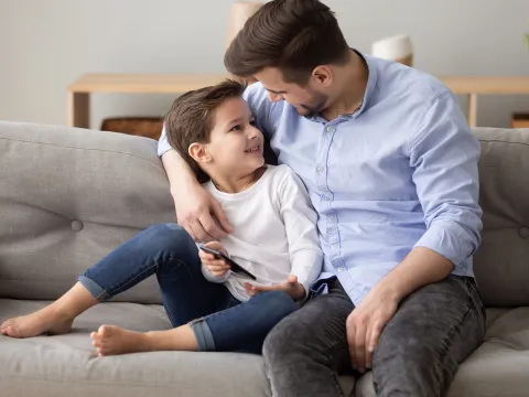 A father talks to his son on the living room couch.