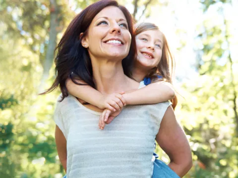 A woman gives her daughter a piggy back ride.