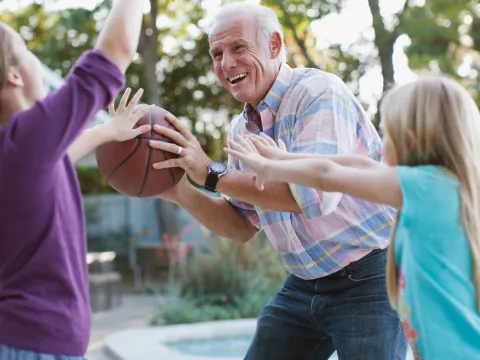 A grandfather plays basketball with his granddaughters. 