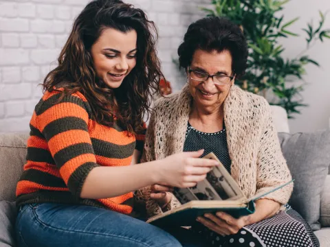 A grandmother and granddaughter look at a photo album together.