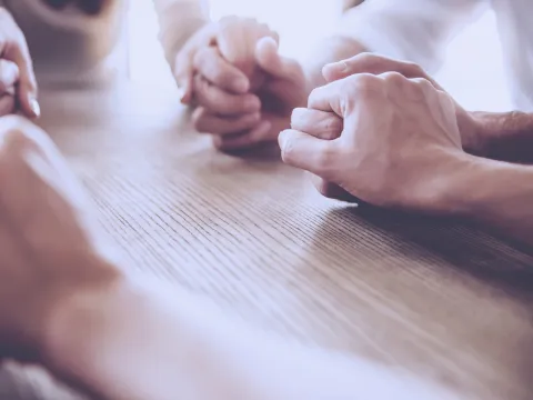 A group of friends holds hands in prayer.