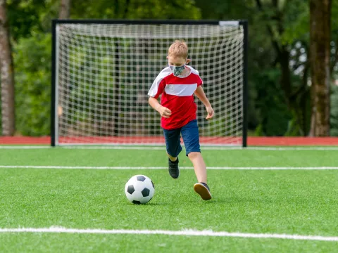 A child playing soccer with his mask on