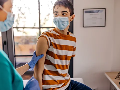 A teenager getting a vaccine shot by a nurse