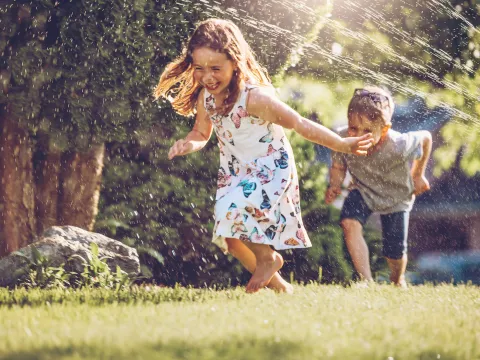 Two children playing in the yard with sprinklers.