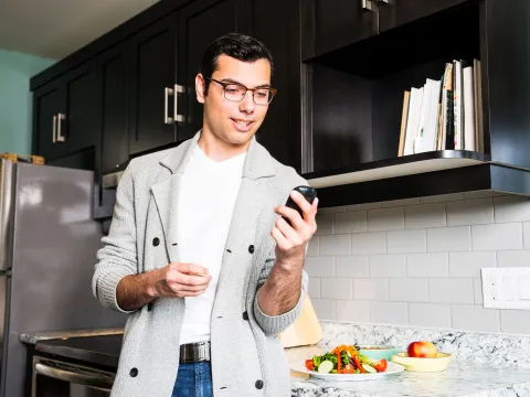 A Man Wearing Glasses Checks His Glucose Levels Before Eating a Healthy Meal in His Kitchen