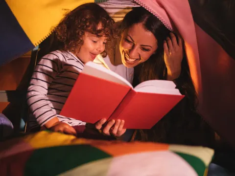 A mom and daughter read together by flashlight.