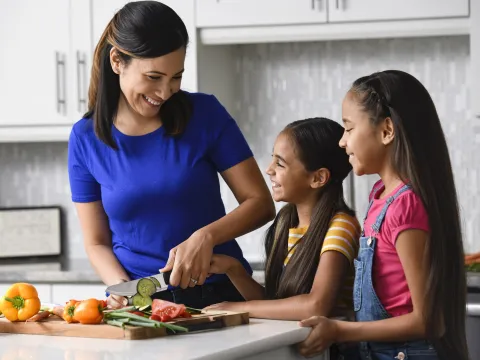 A mom chopping vegetables with her daughters in the kitchen.