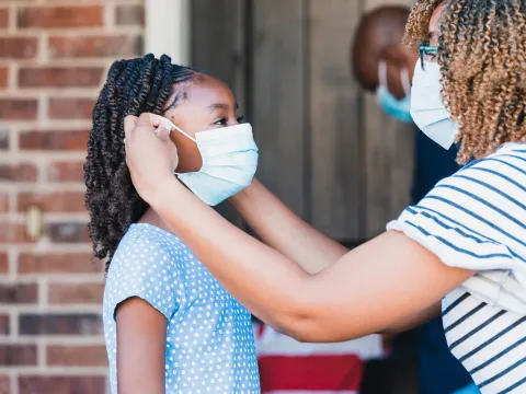 A mom helps her daughter with her face mask.