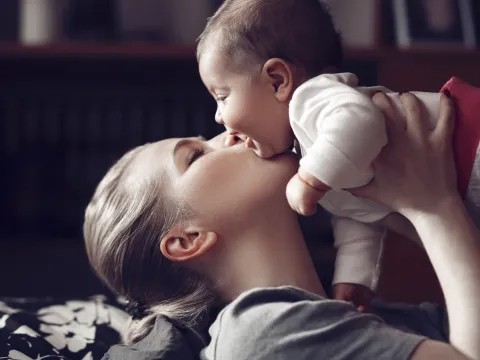 A mom kissing her giggling baby.