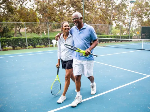 A mature couple laughs together after a lively game of outdoor tennis