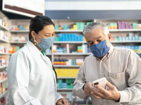 Older man talking with a pharmacist while both wear masks.