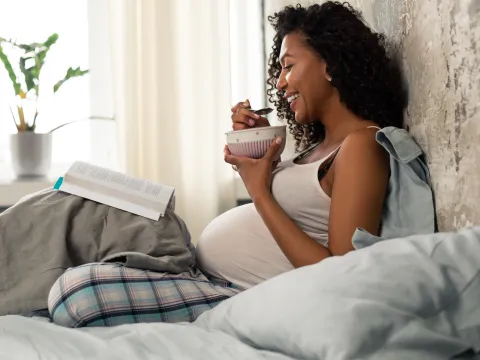 A pregnant woman eating breakfast in bed.