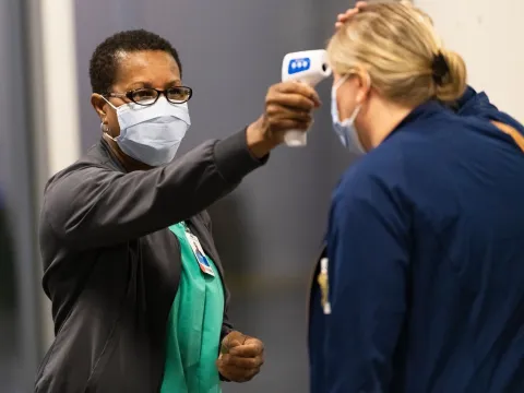 A health care worker temperature testing a patient. 