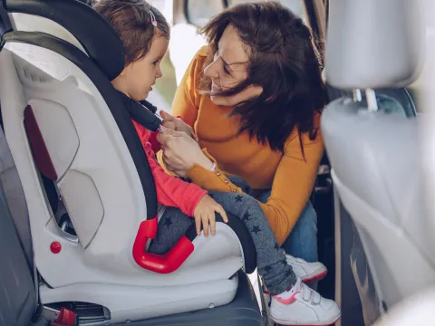 A mom buckles her toddler into her carseat.