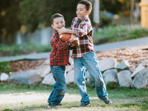 Two young boys playing football outside.