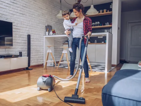 A mom juggles vacuuming the floor with holding her child at her hip.