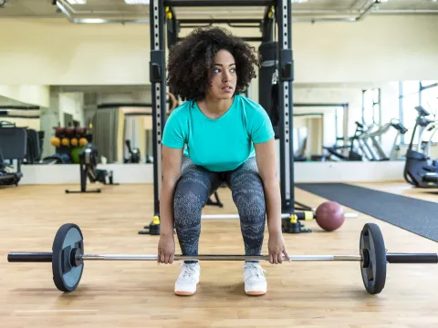 A young black woman lifts a barbell at the gym