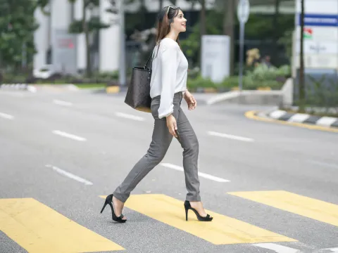 A woman crosses the street wearing high heels.