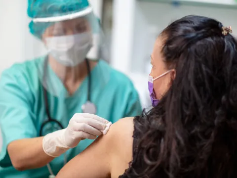 Provider prepping woman to receive a vaccine while they wear PPE and the woman wears a mask.