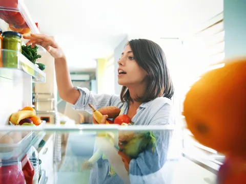 Young woman fills her arms with healthy vegetables at home