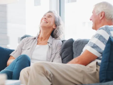 A woman laughing while sitting on the couch with her spouse.