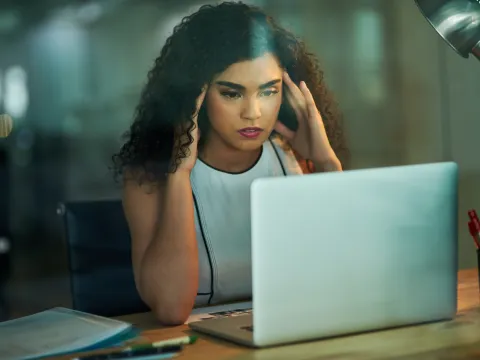 A woman massaging her temples at her desk at work.