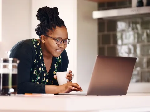 A black woman researches on her laptop while drinking coffee