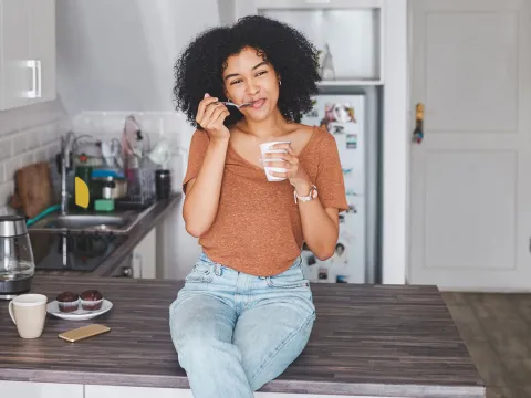 A woman sitting on her counter eating yogurt. 